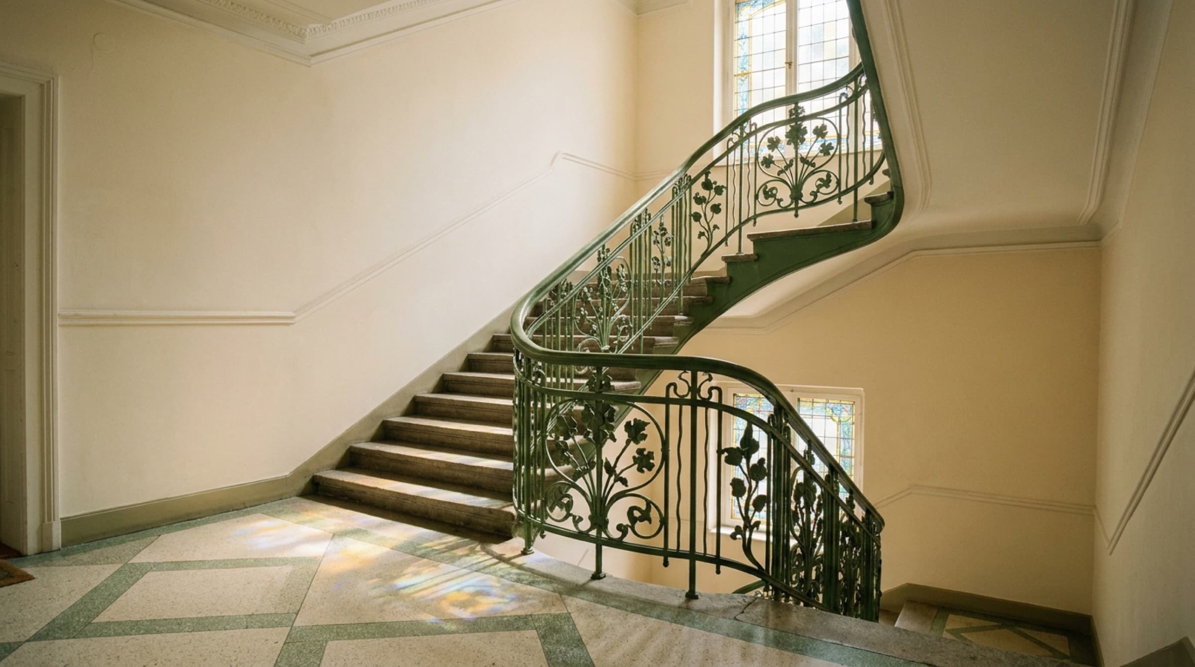 Treppenhaus eines Gründerzeit-Altbaus mit geschwungenem gusseisernem Geländer und weichem Tageslicht
